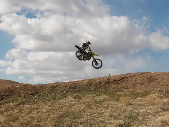 Rider on a yellow dirt bike jumping above a dirt ridge beneath scattered clouds.