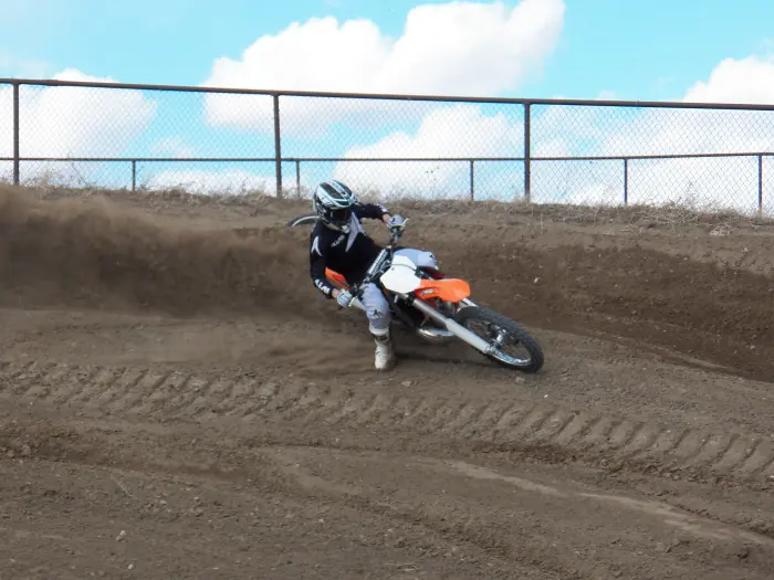 Rider leaning an orange dirt bike through a banked dirt corner.