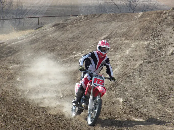 Rider on a red number 112 dirt bike riding toward the camera with dust behind.
