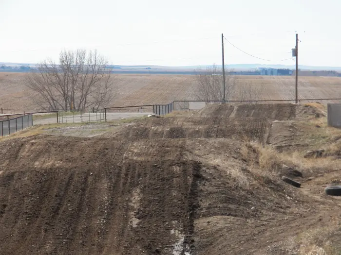 A sequence of dirt jumps at Temple Hill with farmland beyond the fence.